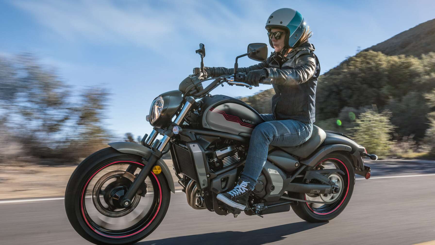 Eine Kawasaki Vulcan S fährt auf einer Straße, im Hintergrund Büsche