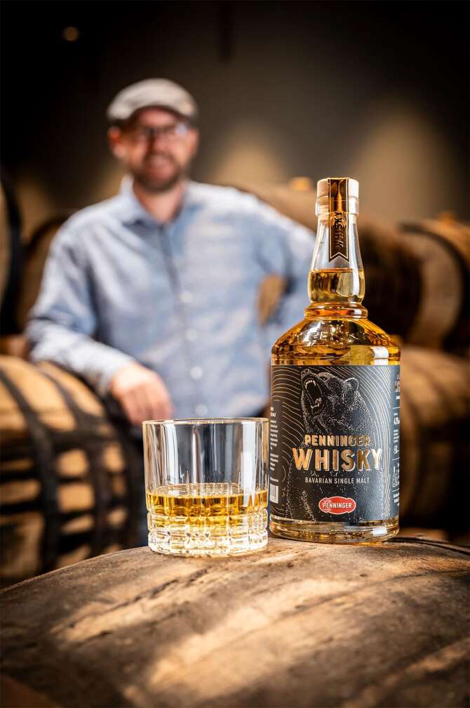 Bild des Penninger Whiskeys mit Whiskeyfass und Stefan Penninger unscharf im Hintergrund