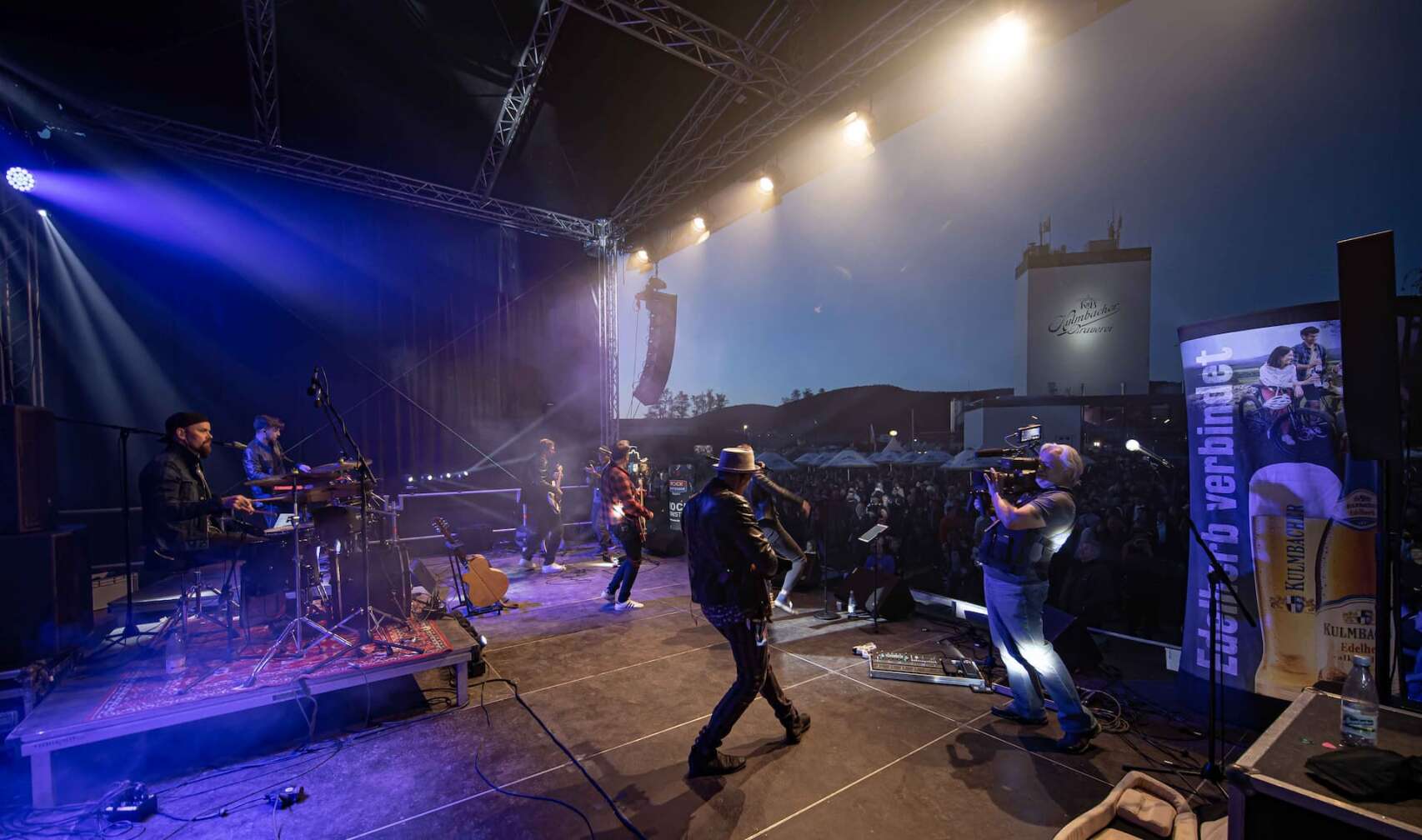 Die ROCK ANTENNE Band tritt bei der Motorradsternfahrt Kulmbach auf. Blick vom hinteren Rand der Bühne auf die Band und das Publikum.