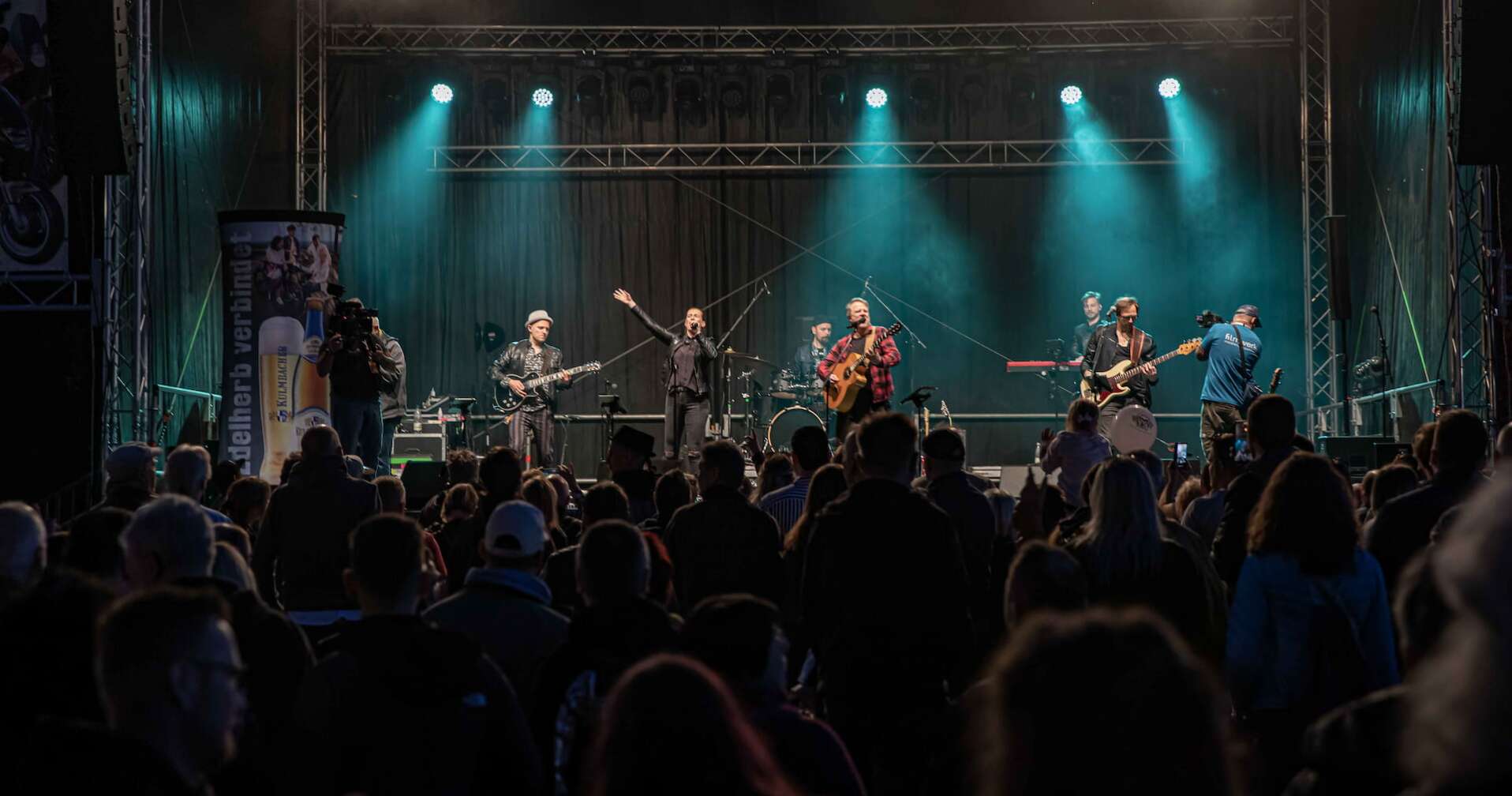 Die ROCK ANTENNE Band tritt bei der Motorradsternfahrt Kulmbach auf. Blick von hinten aus dem Publikum auf die Bühne.