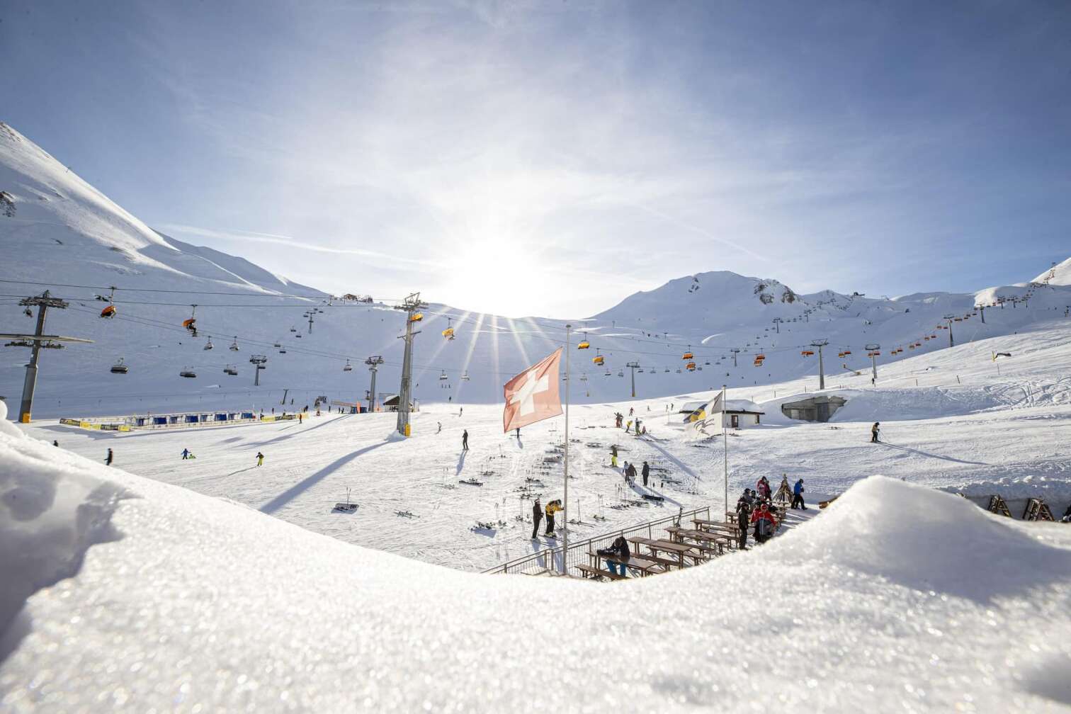 Foto einer Skihütte mit wehender Schweiz-Flagge vor dem herrlichen Panorama der schneebedeckten Berge in der Silvretta Arena in Samnaun/Ischgl